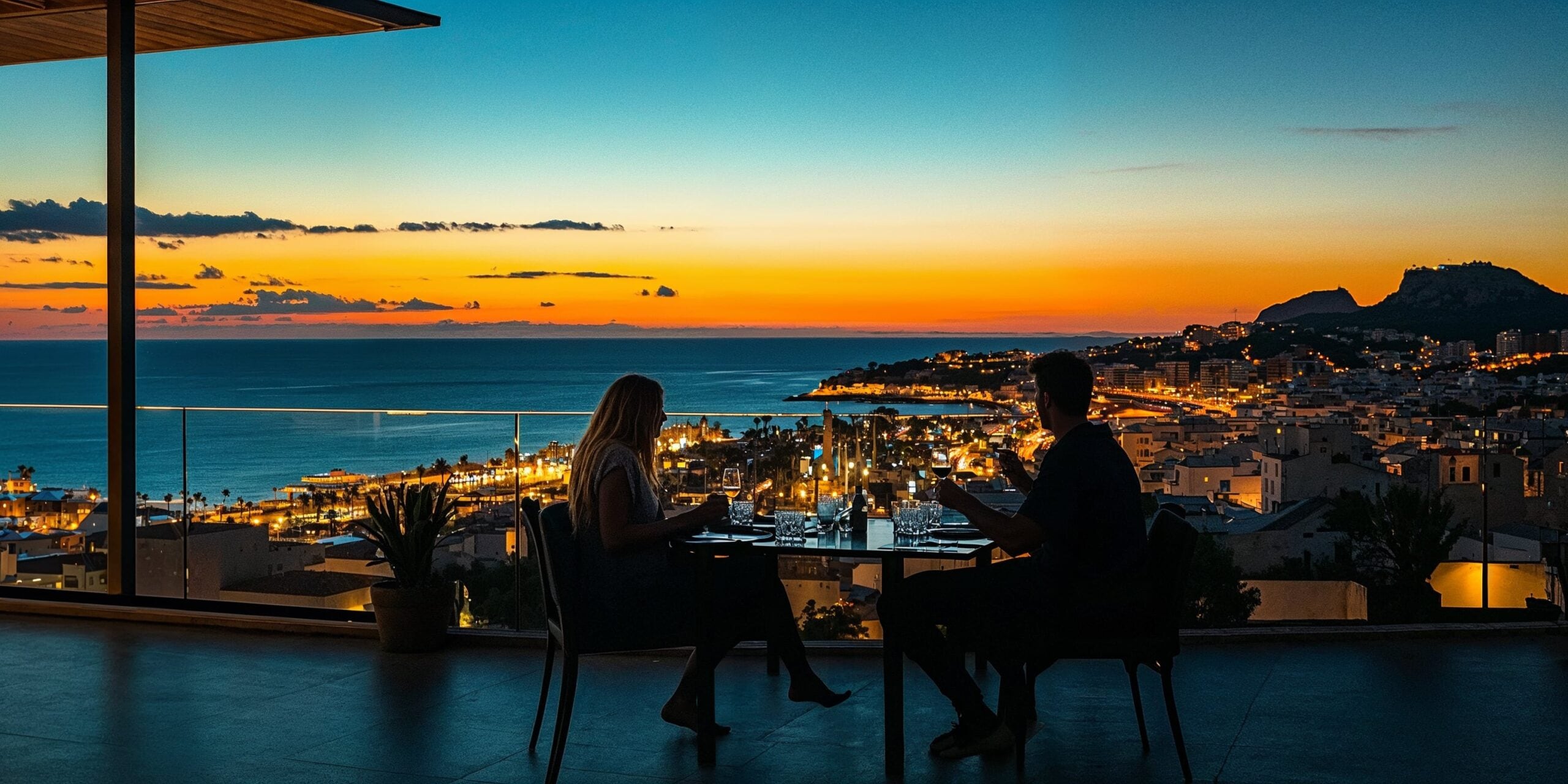 A couple who is Investing in Spanish property is dining on a rooftop with a view of the ocean and city lights | SunnyCasas