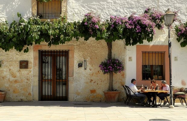 Charming scene in San Miguel de Salinas with diners enjoying a meal outdoors under vibrant flowers and a rustic building.